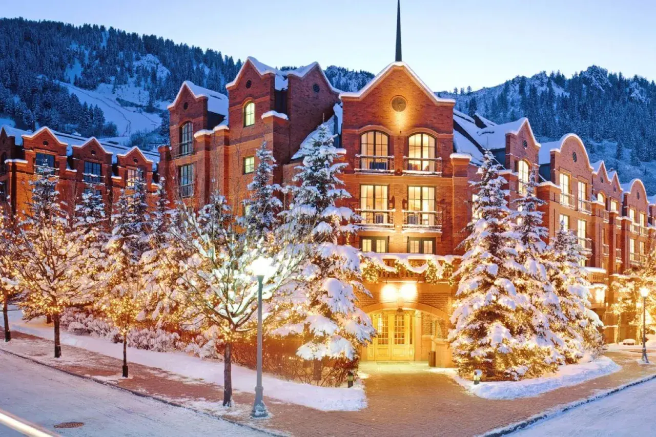 Luxuriöses Hotel im teuersten Skigebiet der Welt, umgeben von verschneiten Bäumen mit Lichterketten und Bergen im Hintergrund.