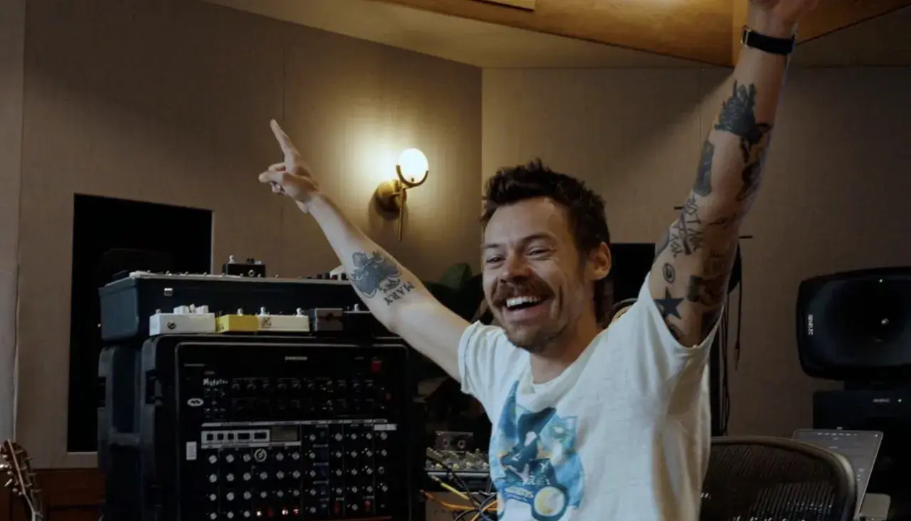 Harry Styles w studiu nagraniowym, z rękami w górze, przygotowuje się do kolejnego koncertu.