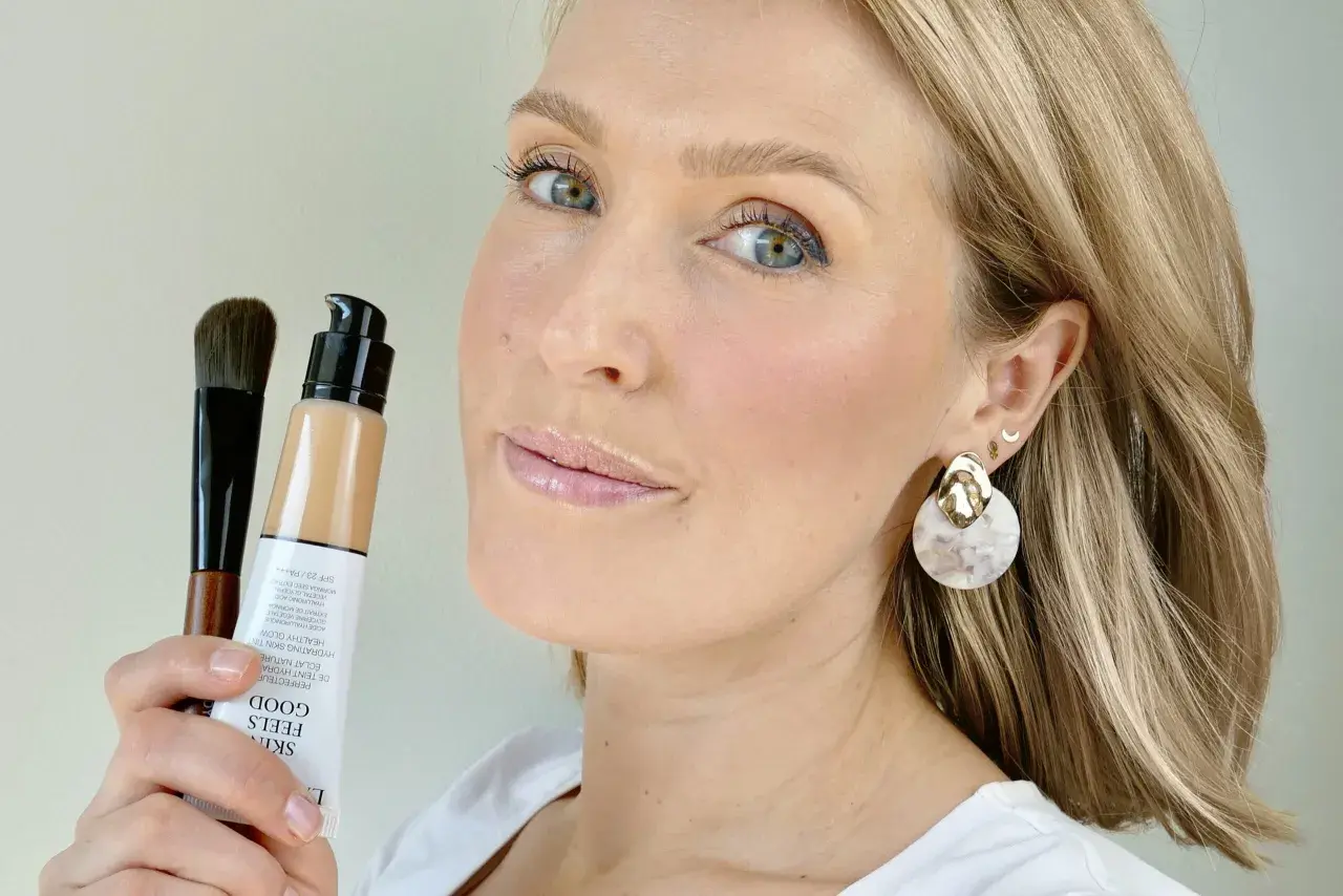 En kvinna håller upp en flaska Giorgio Armani foundation och en borste. Hennes hud ser naturligt fräsch ut.
