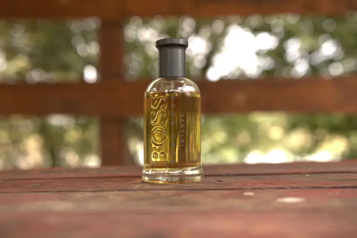 Szklana butelka perfum Boss Bottled Intense, z płynem o bursztynowym kolorze, stoi na drewnianym stole.