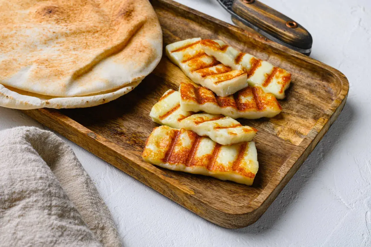 Des morceaux de halloumi grillé, marqués par les rayures du grill, reposent sur un plateau en bois à côté d'un pain pita moelleux.