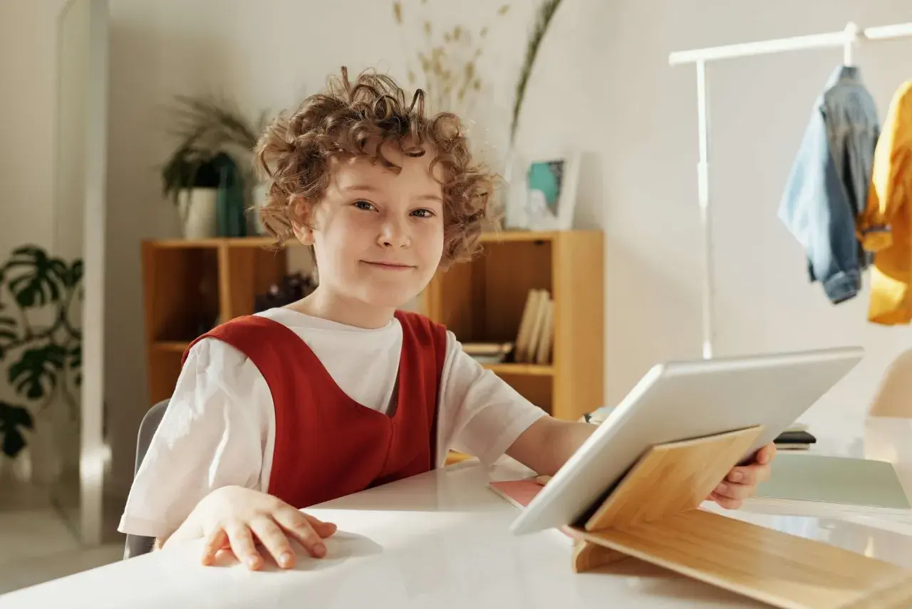Chłopiec z kręconymi włosami uśmiecha się, trzymając tablet. Czy to wady i zalety szkoły waldorfskiej?