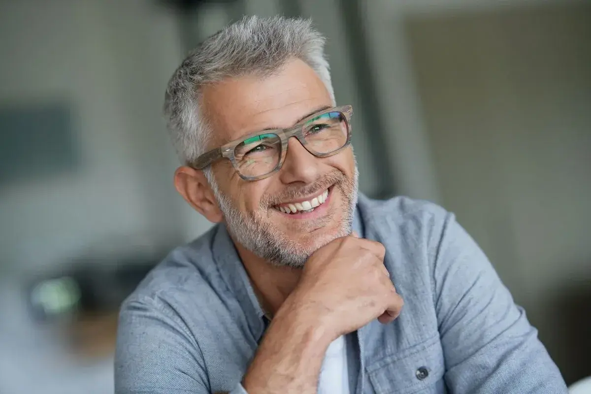 Lächelnder Mann mit Brille und grauem Haar, ein Beispiel für moderne herren frisuren ab 50.