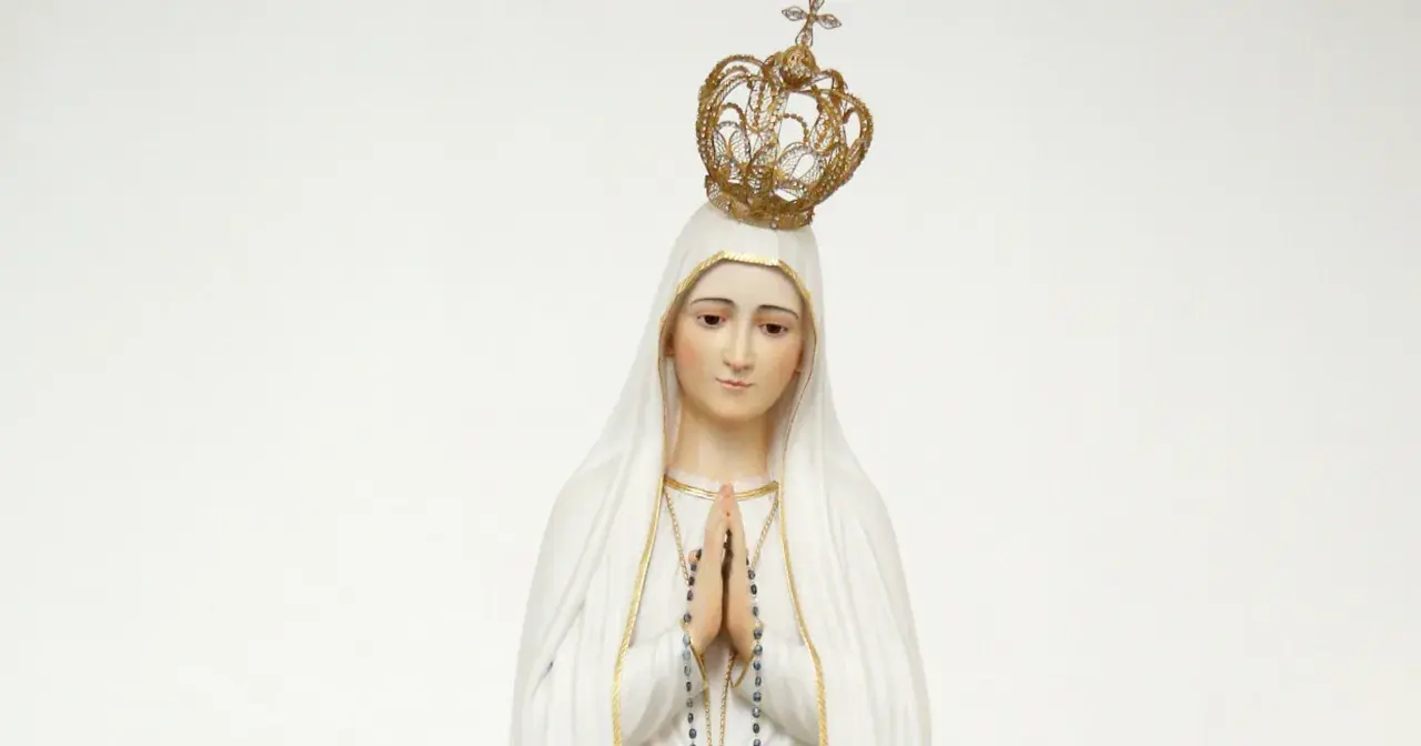 Figurka Matki Bożej Fatimskiej w białym welonie i złotej koronie, z rękami złożonymi do modlitwy.
