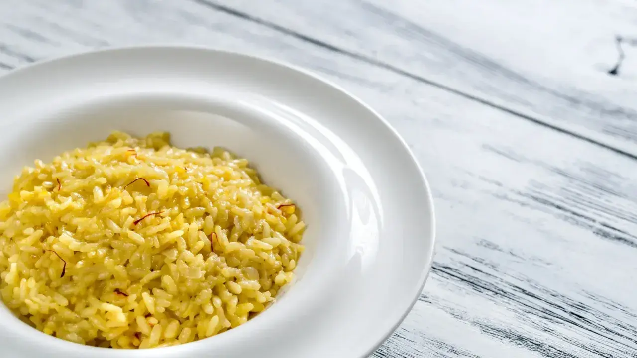 Un crémeux risotto à la milanaise, parsemé de fils de safran, dans une assiette blanche sur fond de bois.