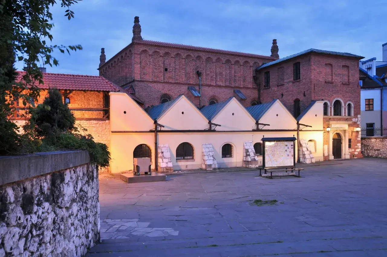 Stara synagoga w Krakowie o zmierzchu. Ceglana fasada, jasne przybudówki i kamienny dziedziniec tworzą historyczny klimat.