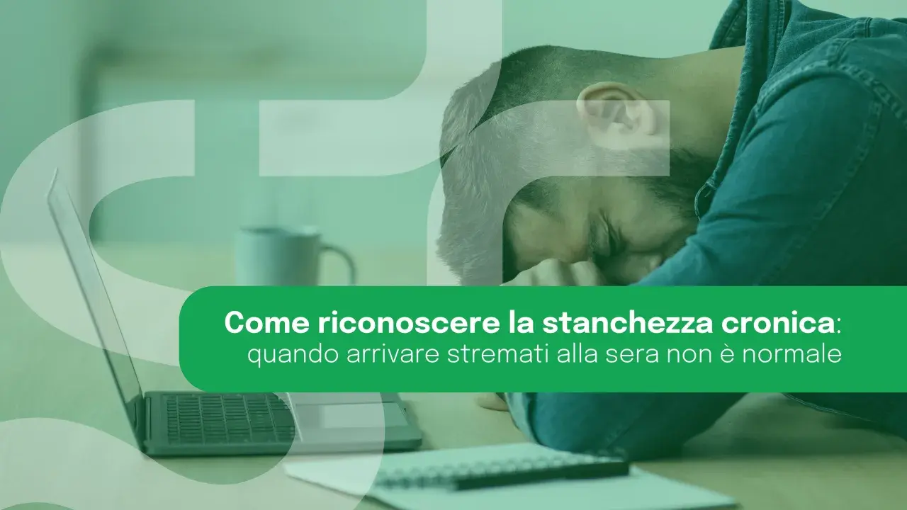 Uomo esausto appoggiato alla mano, con laptop e taccuino. La stanchezza cronica può manifestarsi anche con un senso di spossatezza serale.