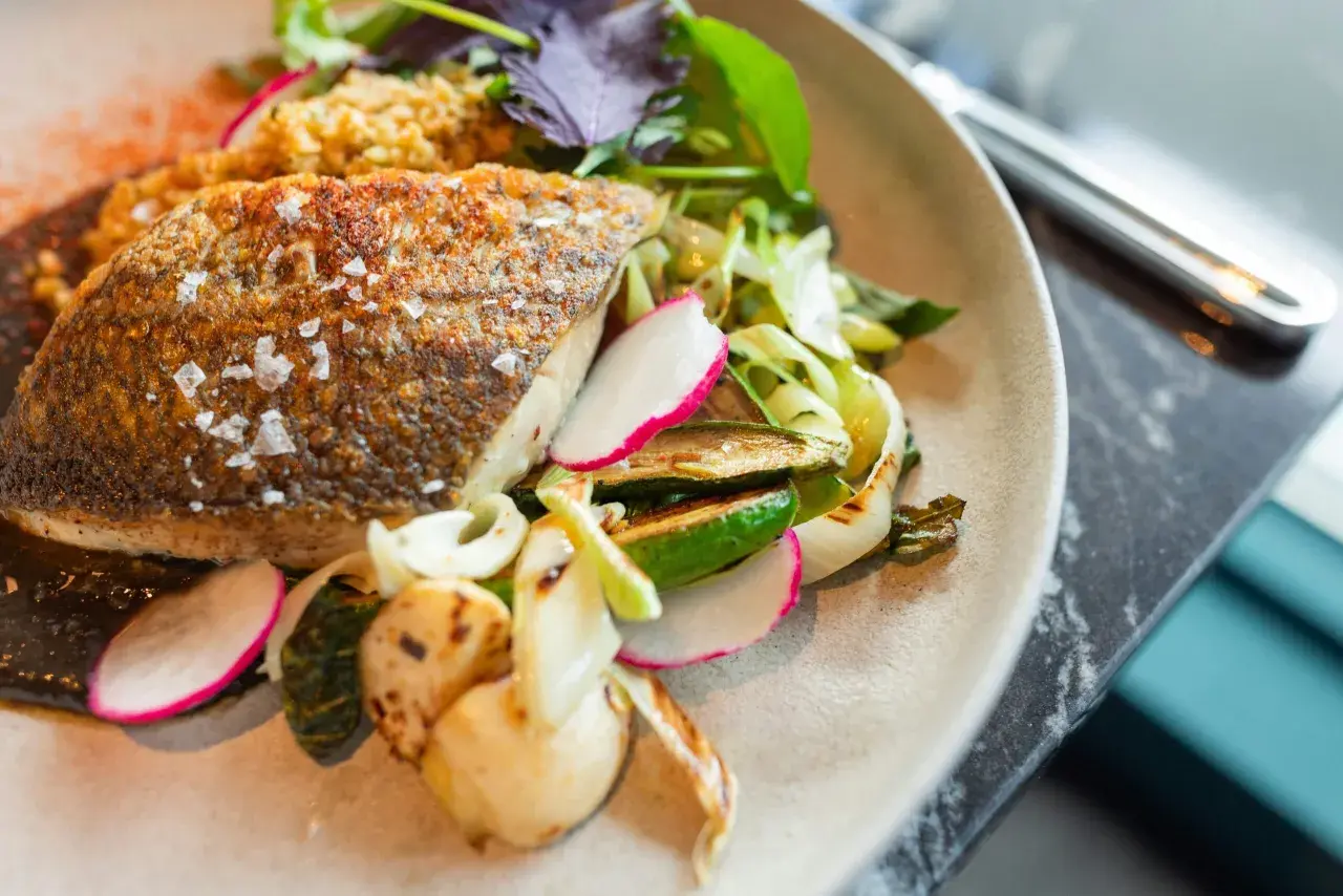 Delicioso pescado blanco crujiente con guarnición de verduras a la parrilla y rábano fresco.