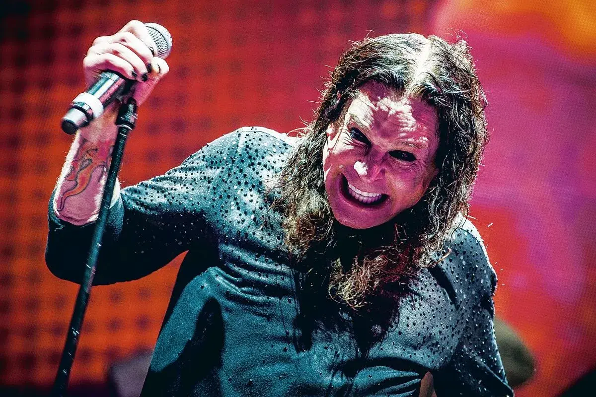 Ozzy Osbourne, wokalista Black Sabbath, z mikrofonem w dłoni, z charakterystycznym wyrazem twarzy na koncercie.