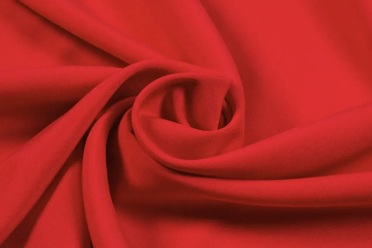 Roter Stoff, der sich zu einer Spirale drapiert. Die Textur ist glatt, was auf Lyocell oder Viskose hindeutet. Der Unterschied zwischen Lyocell und Viskose ist oft subtil.