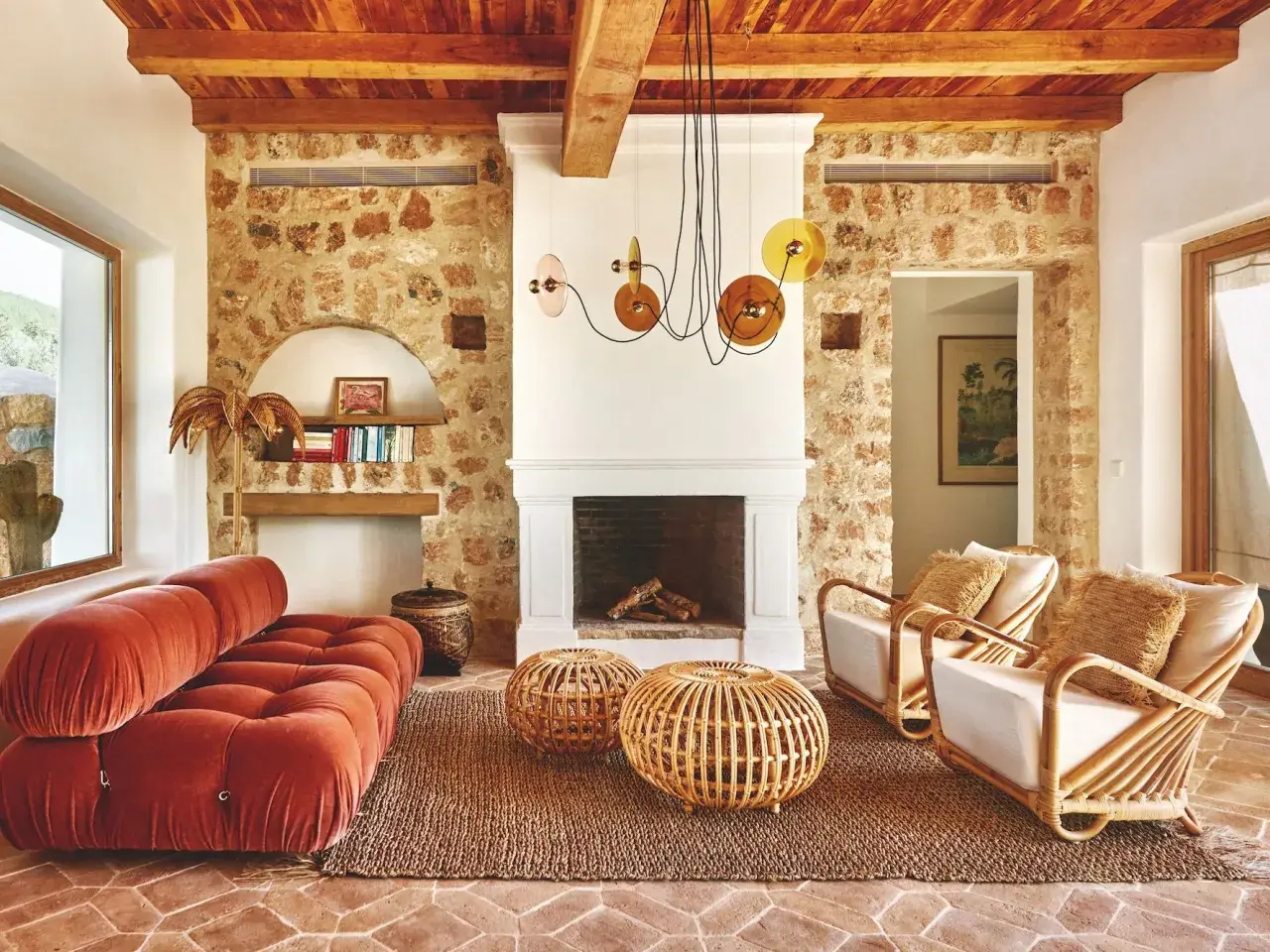 Gemütliches Wohnzimmer im Boho-Stil mit Terrakotta-Boden, Steinwand, Korbmöbeln und einem roten Samtsofa. Die boho bedeutung zeigt sich in der entspannten Atmosphäre.