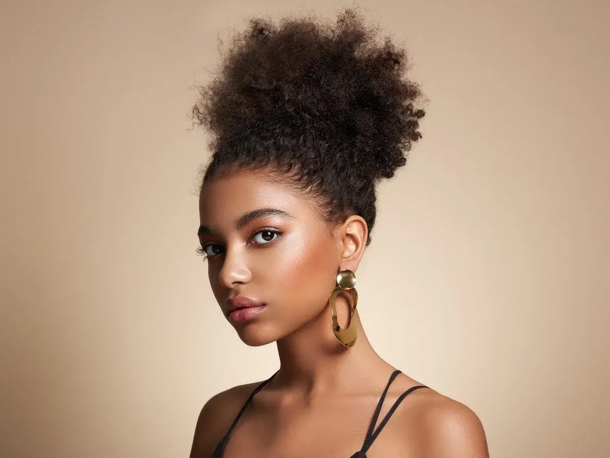 Joven con peinado afro y grandes pendientes dorados, luciendo unos estilos de maquillaje que realzan su belleza natural.