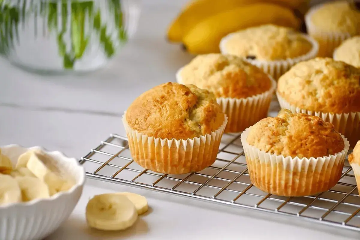 Frisch gebackene bananen muffins auf einem Gitter, daneben eine Schüssel mit Bananenscheiben.
