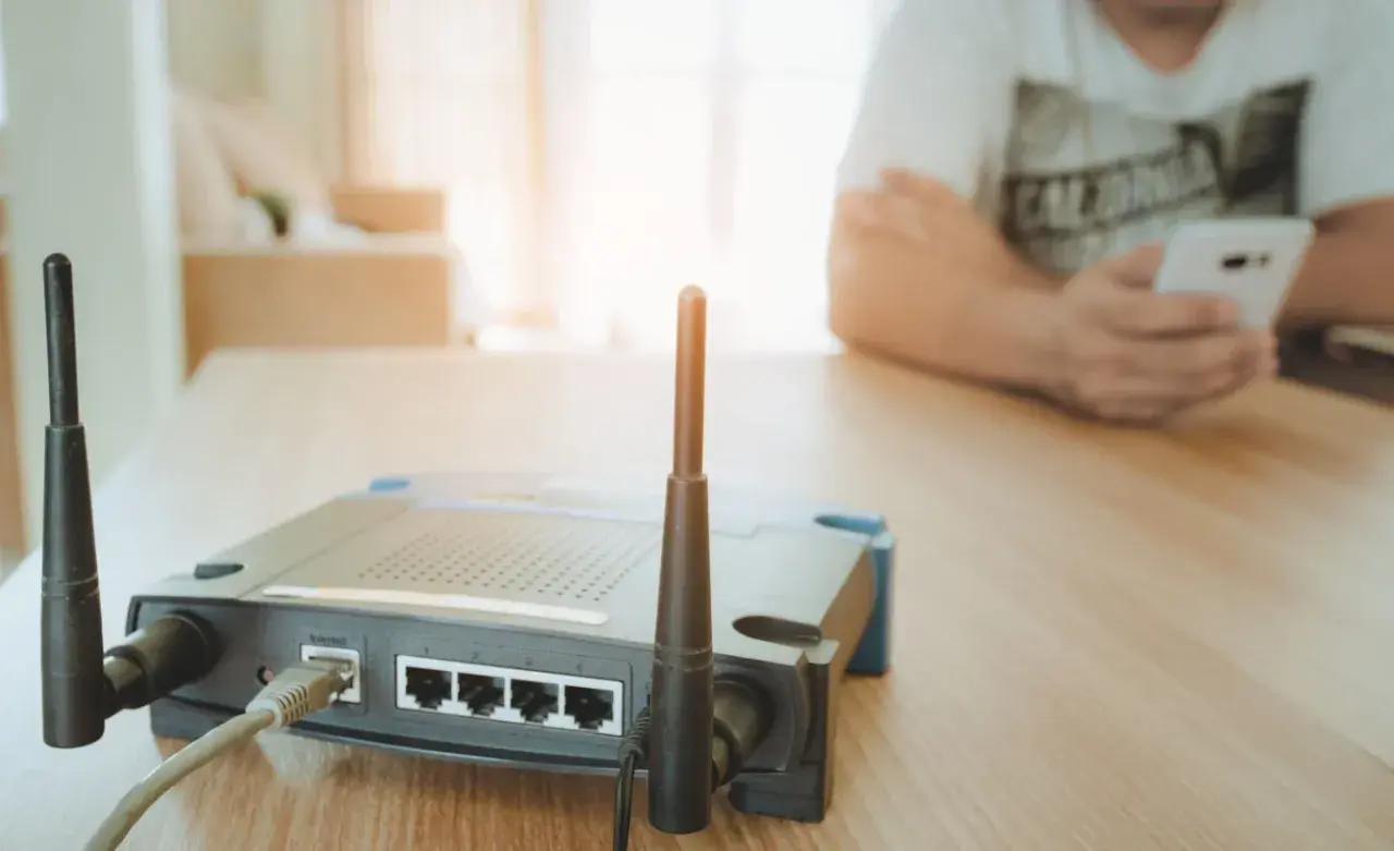 Router z antenkami tworzy domowy hotspot. W tle osoba korzysta z telefonu.