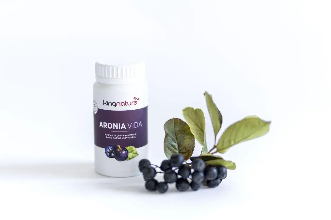 Flasche "ARONIA VIDA" mit Aronia-Extrakt und Vitamin C, daneben frische Aroniabeeren mit Blättern.