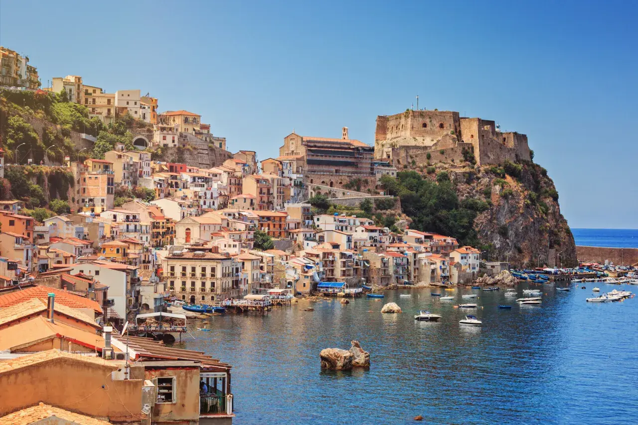 Colorful houses cascade down a cliffside to a harbor filled with boats, overlooking the sea. This is one of the picturesque cities in Calabria, Italy.