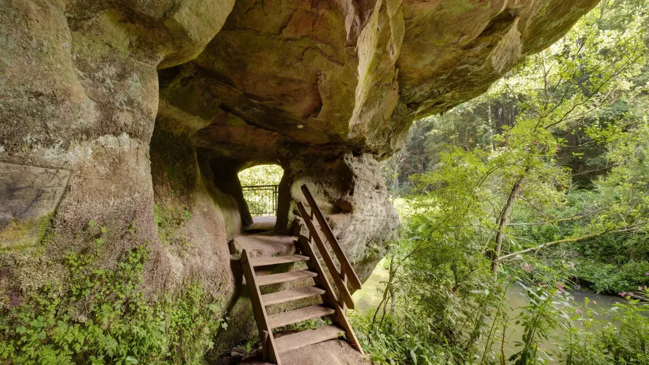 Holztreppe führt aus einer Felsgrotte auf dem schwarzachklamm wanderweg. Ein Fluss plätschert im Hintergrund.