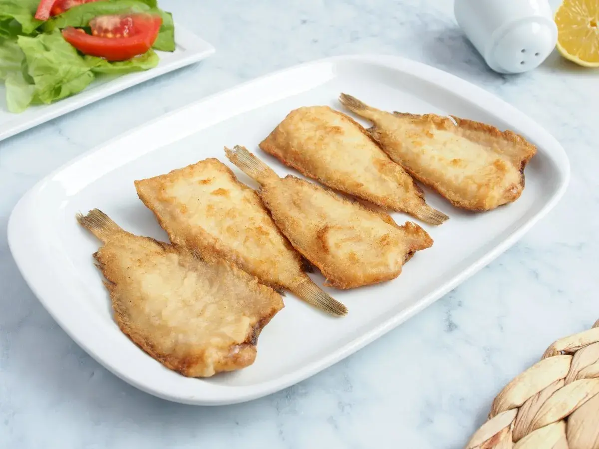 Cinco acedias fritas doradas y crujientes en un plato blanco, listas para disfrutar.