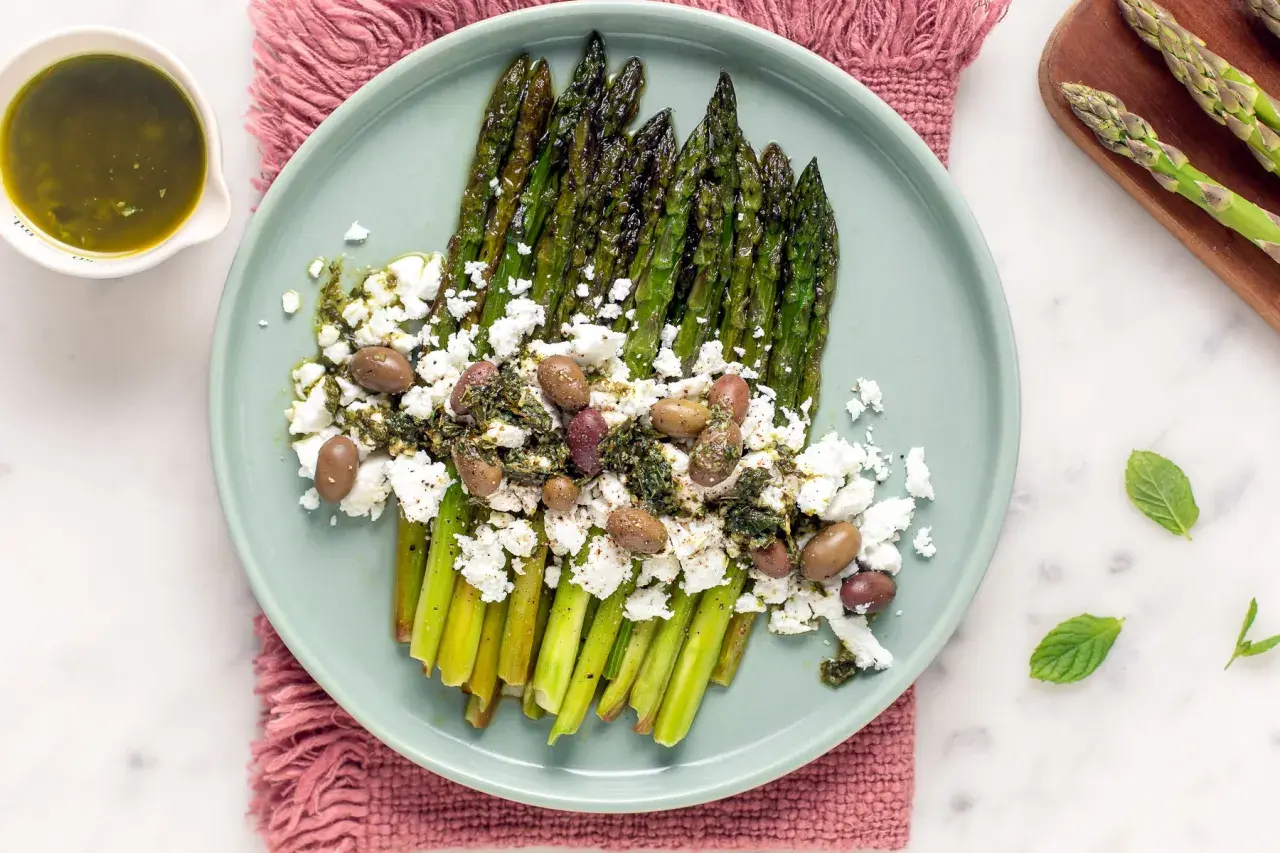 Asparagi grigliati con formaggio simile alla feta, olive e salsa verde. Un piatto fresco e saporito.