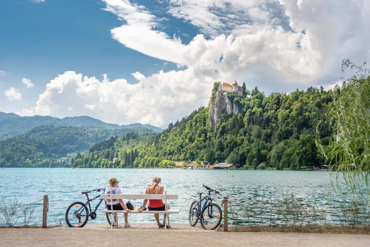 Para odpoczywa na ławce, podziwiając zamek na skale nad jeziorem Bled. Idealne miejsce na camping Bled Slovenia.
