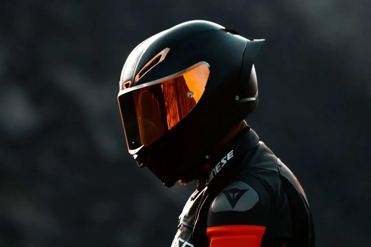 Motociclista con casco integral deportivo, uno de los tipos de cascos de moto, con visor naranja reflectante.