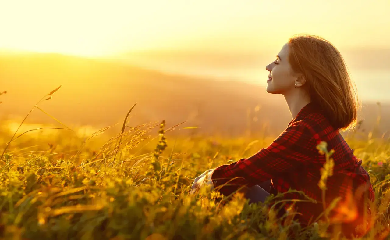 Mujer sonríe en un campo al atardecer, disfrutando de la paz y fortaleciendo su autoestima personal.