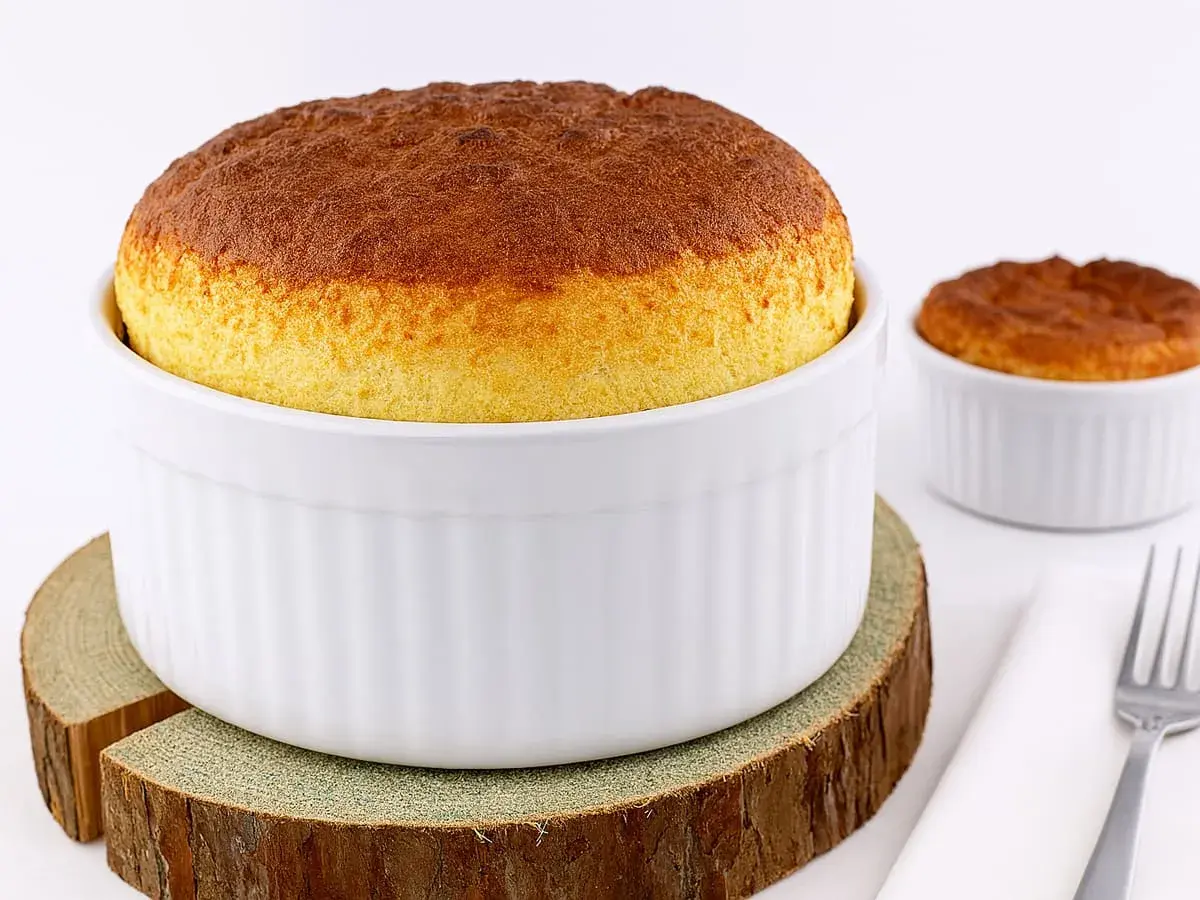 Deux soufflés au fromage dorés, prêts après leur temps de cuisson. L'un est dans un grand ramequin blanc, l'autre dans un plus petit.