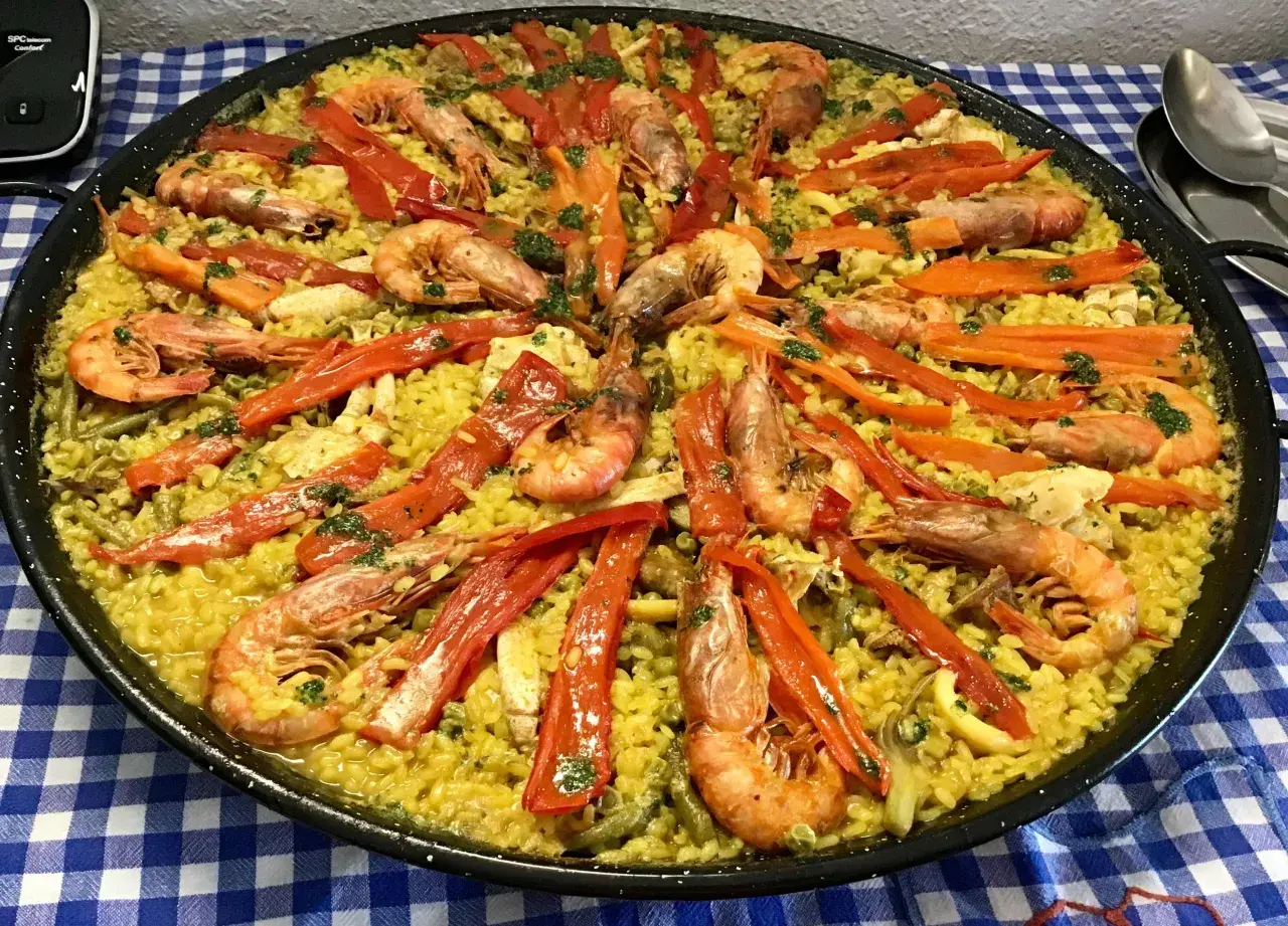 Paella mar y montaña, un festín de arroz amarillo con gambas, pimientos rojos y verduras.