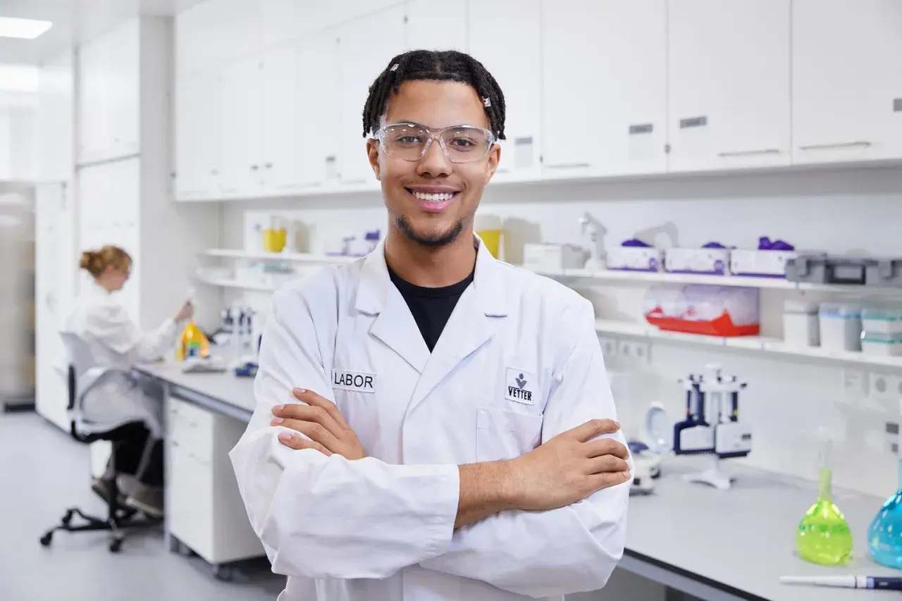 Junger Mann im Chemielabor, bereit für neue chemielaborant stellenangebote. Im Hintergrund eine Kollegin bei der Arbeit.