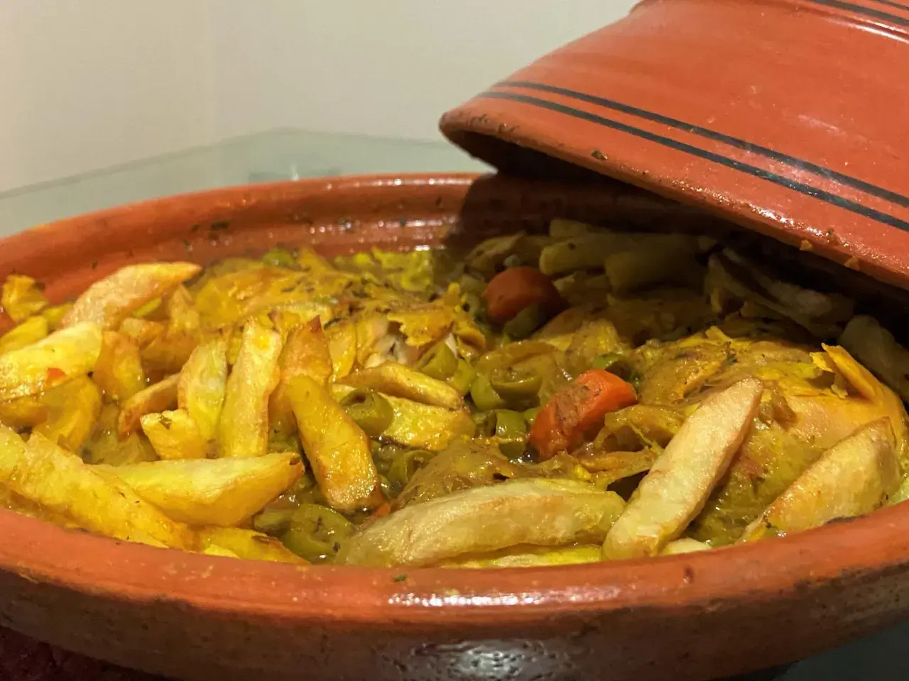 Un plat de tajine poulet olive, avec des pommes de terre dorées et des carottes, prêt à être dégusté.
