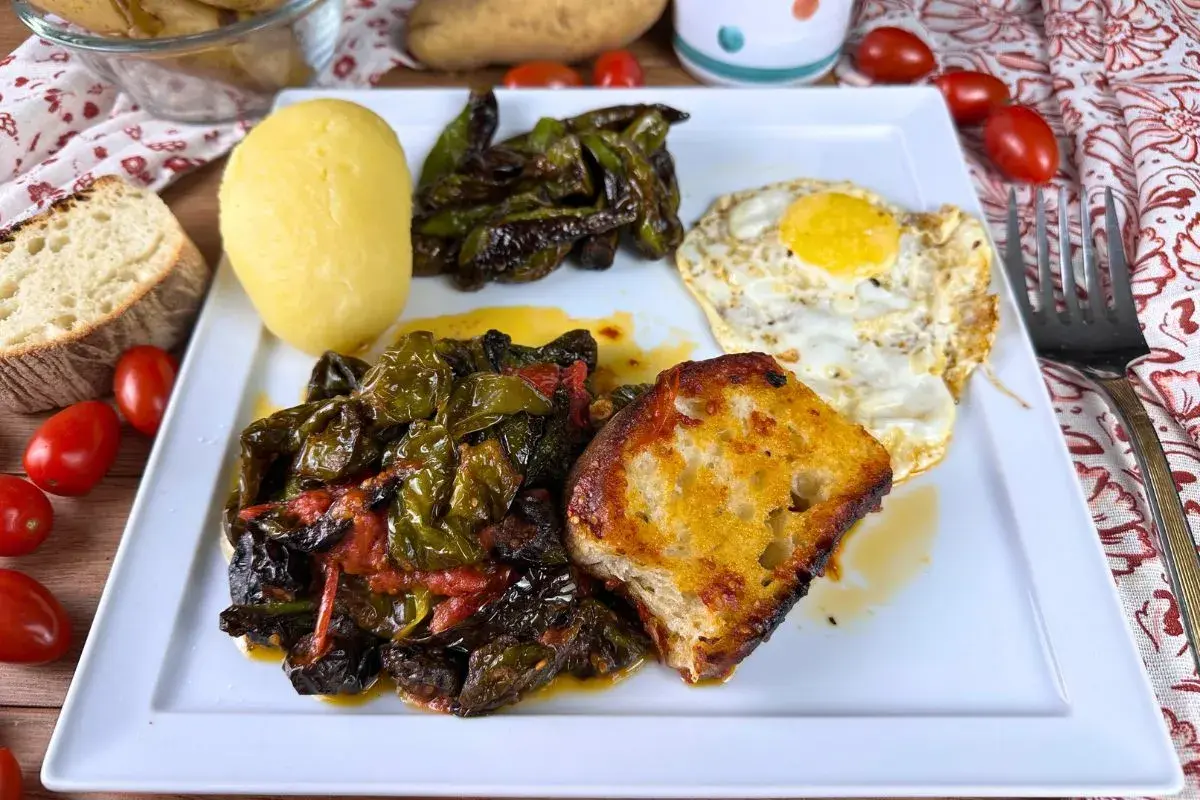 Piatto con friggitelli in padella, uovo fritto, patata lessa, pane tostato e pomodorini.