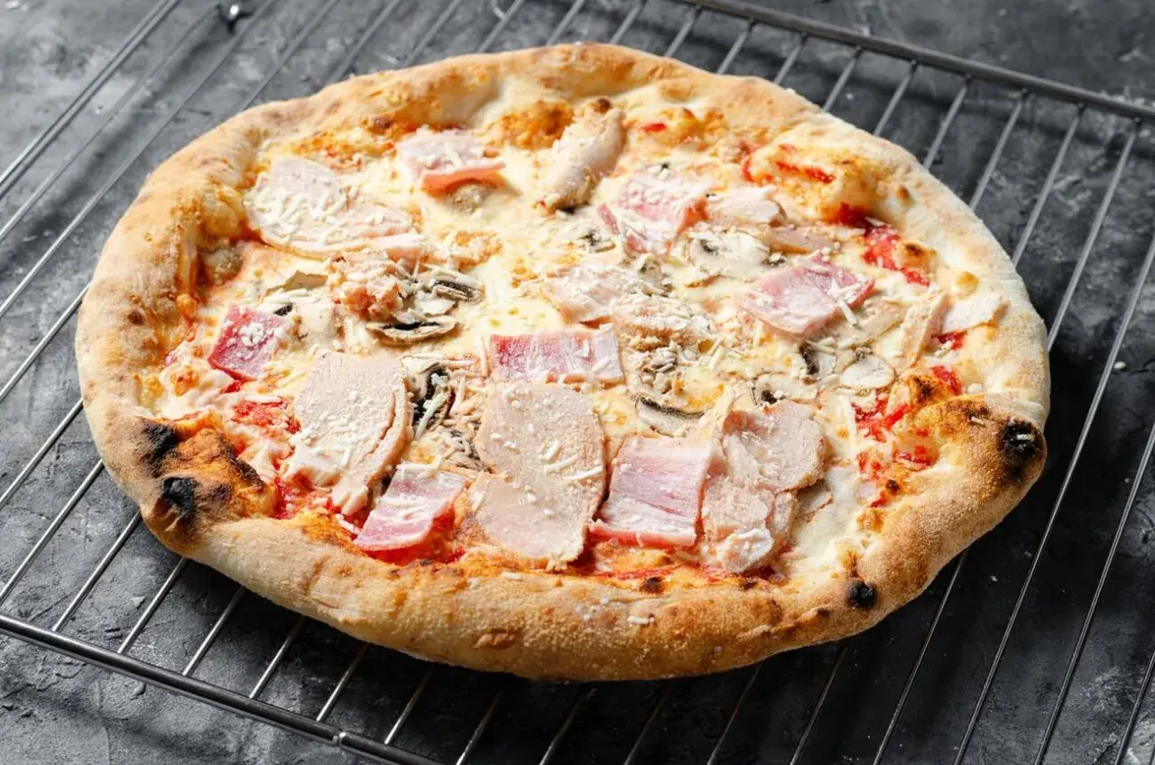 Eine knusprige Pizza mit Schinken und Pilzen auf einem Gitterrost.