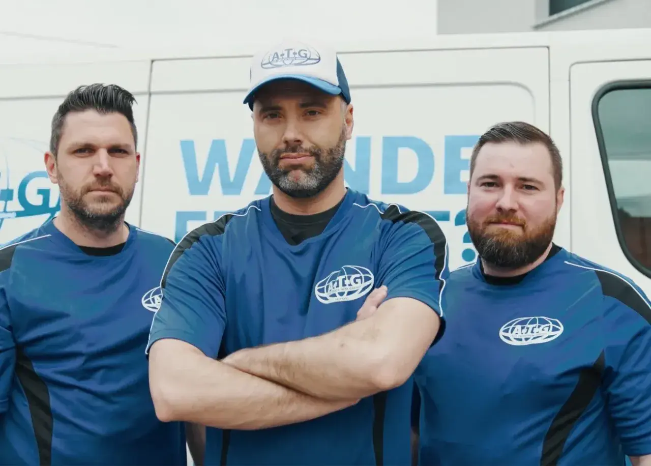 Drei Männer in blauen Arbeits-T-Shirts stehen vor einem weißen Transporter. Sie sind Teil des ATG-Teams, das sich auf Mauertrockenlegung spezialisiert hat.