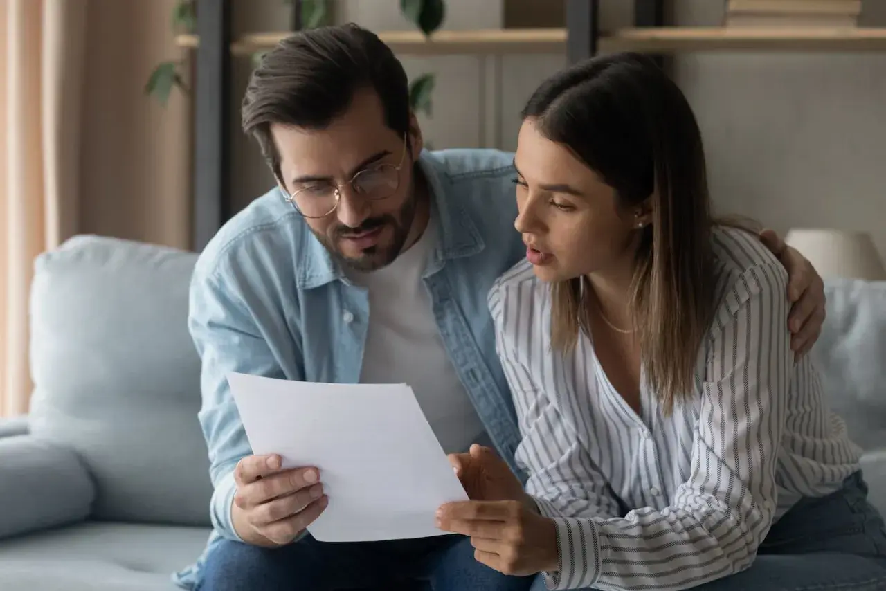 Pareja revisando un documento importante, quizás donde se firma la fein. Él la abraza mientras ambos se concentran en el papel.