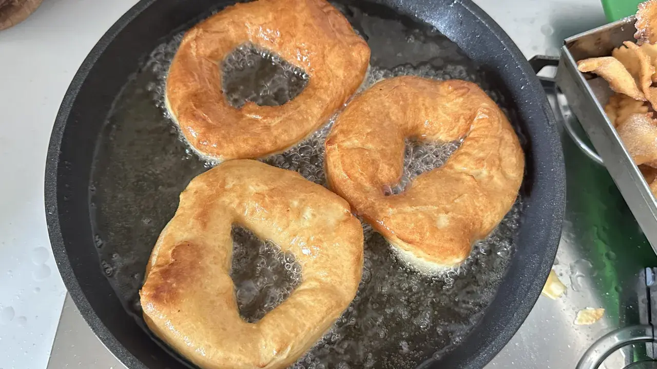 Tre ciambelle fritte dorate sfrigolano nell'olio caldo, pronte per essere gustate.