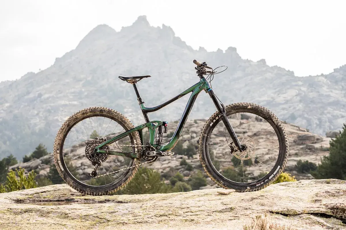 A 2020 Giant Reign mountain bike rests on a rocky outcrop, ready to conquer the rugged, misty mountains in the background.