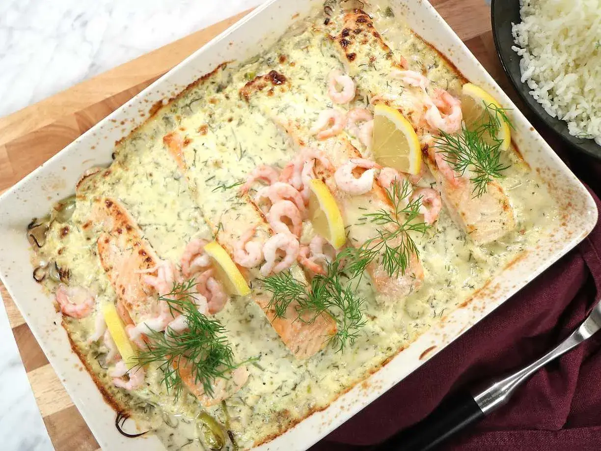 Lax med apelsinsås, toppad med räkor och citronklyftor, serveras i en ugnsform. Dillkvistar ger en fräsch touch.