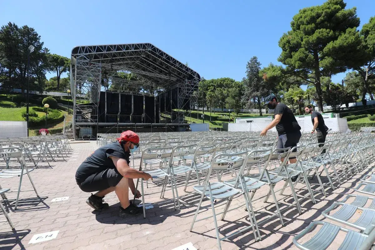 Preparando el escenario para conciertos en el Jardín de Invierno de Zaragoza. Hombres colocan sillas metálicas en filas.