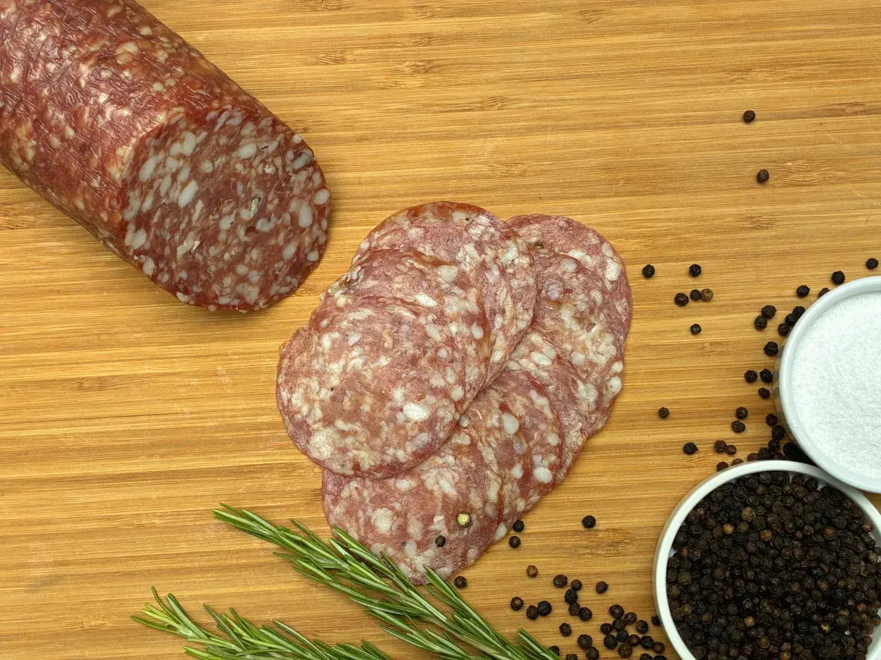 Kawałek salami napoli i kilka plastrów na desce z rozmarynem, pieprzem i solą.