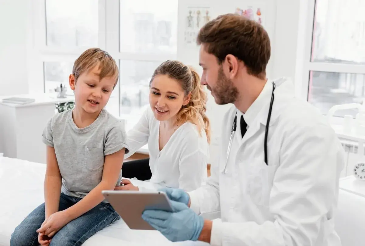 Medico di famiglia: gli orari, le nuove regole. Un dottore mostra un tablet a un bambino e sua madre, spiegando le novità.