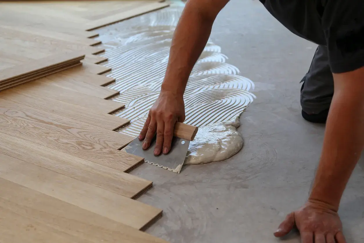 Mano stende colla per parquet incollato. Listelli di legno pronti per essere posati.