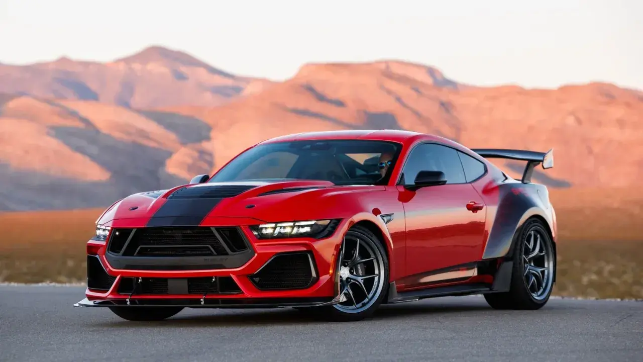 Czerwony mustang shelby z czarnymi pasami i spojlerem na tle pustynnych gór.
