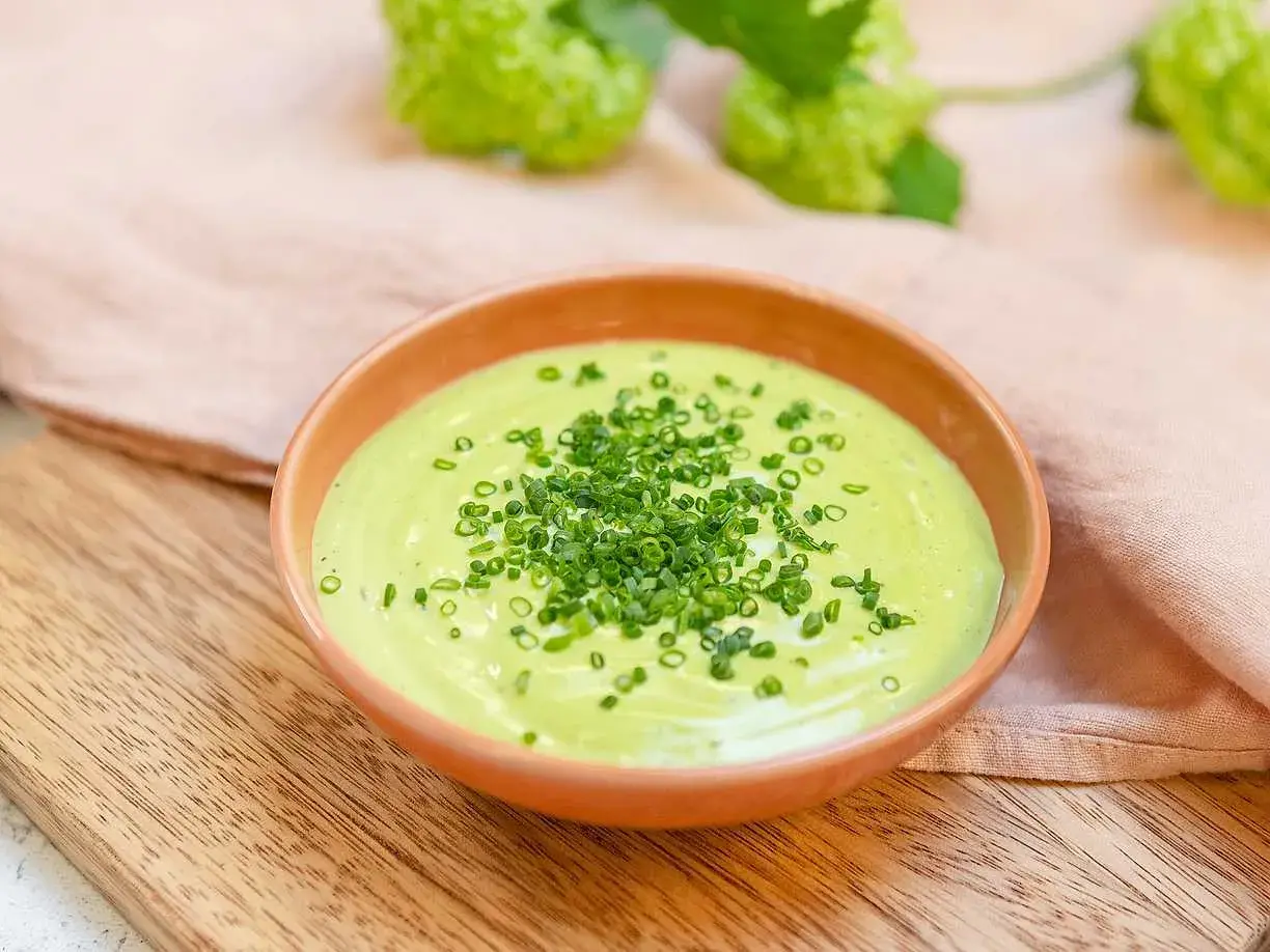 Grön, krämig salsa verde toppad med finhackad gräslök i en skål på en träskärbräda.