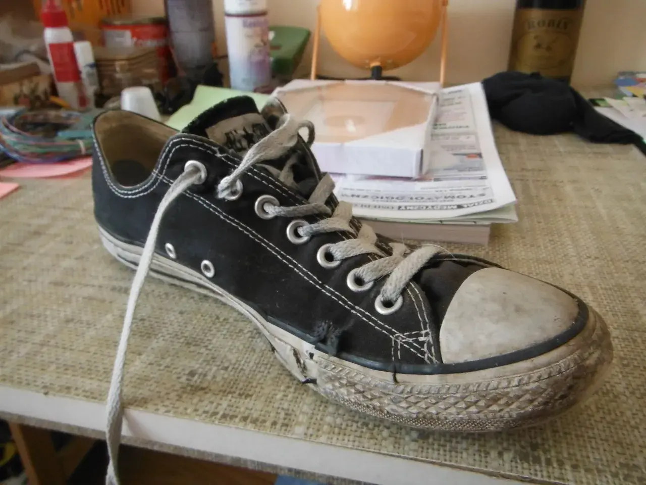 Une chaussure Converse noire usée, avec la semelle qui se décolle, témoigne de nombreuses aventures.