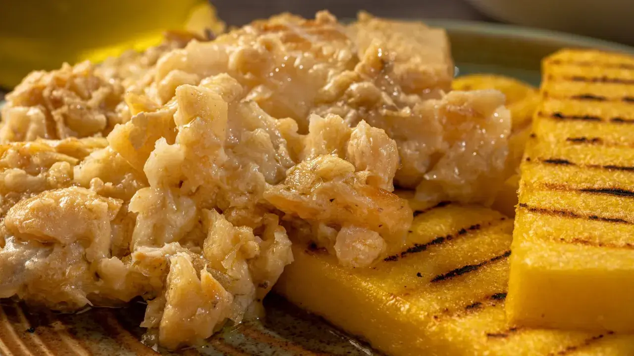 Un saporito baccalà alla vicentina, cremoso e profumato, servito su fette di polenta grigliata.