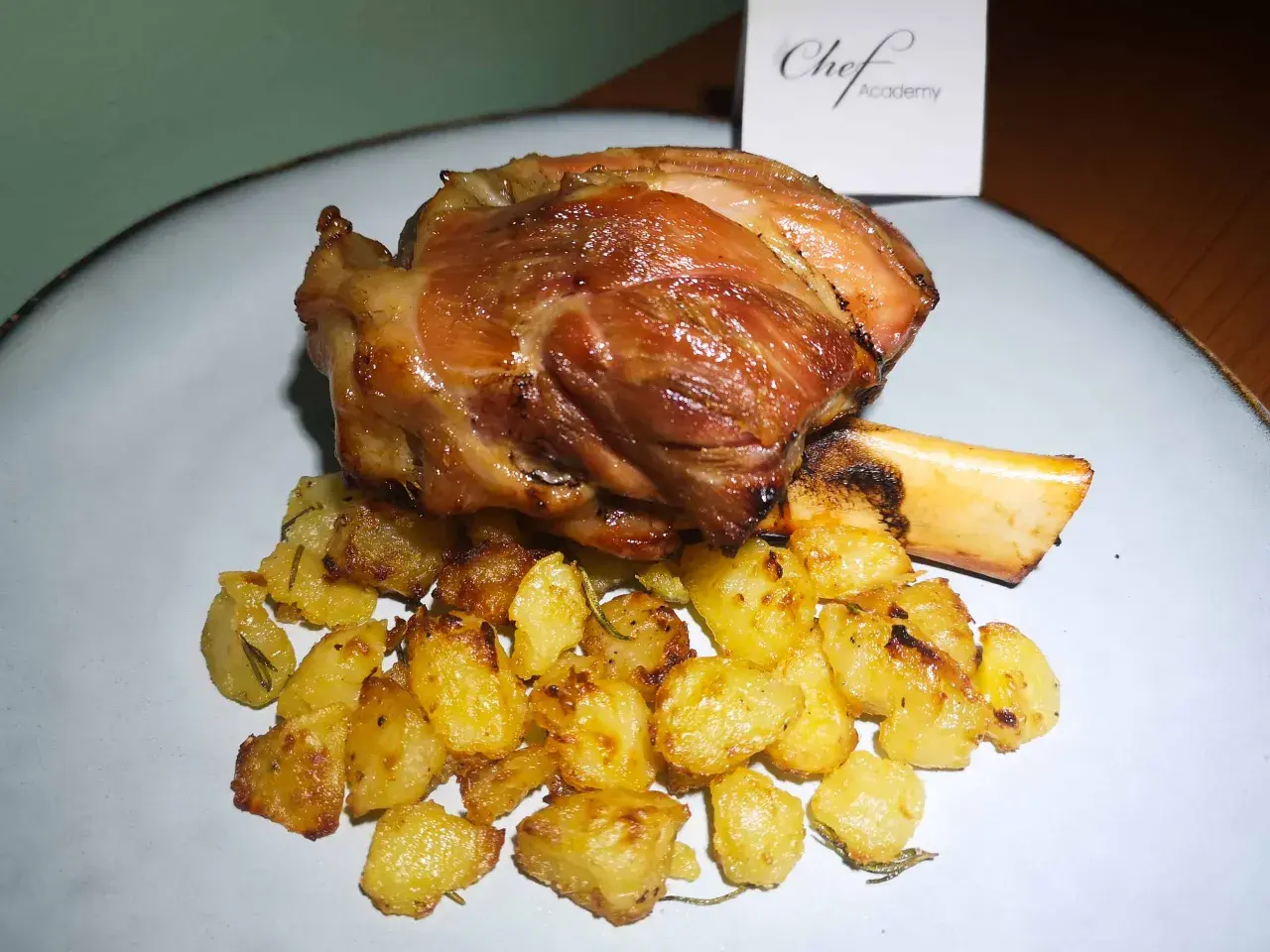 Stinco di maiale succulento e dorato, servito con patate arrosto croccanti e profumate al rosmarino.