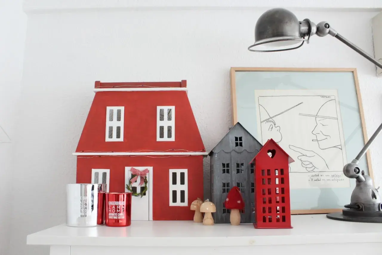 Un pueblo de casitas de navidad de madera, con una casa roja grande y otras más pequeñas, adornos y velas.