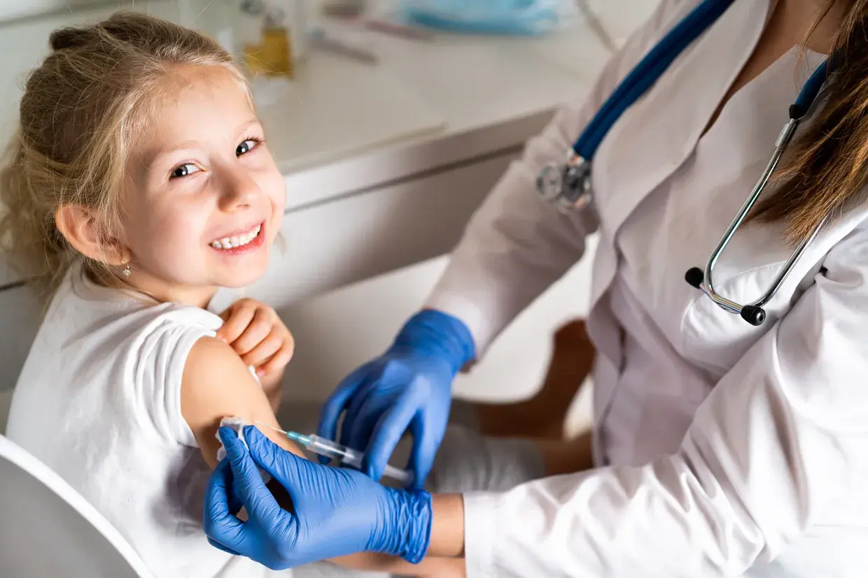 Niña sonriente recibe vacuna contra la gripe. Es recomendable vacunar a los niños de la gripe para proteger su salud.