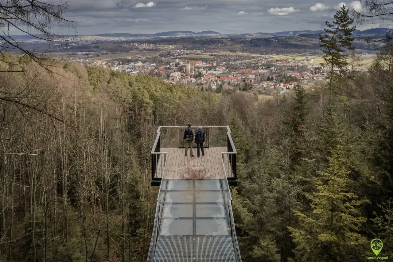 Dwie osoby stoją na szklanym tarasie widokowym, podziwiając panoramę Starego Sącza. To jedna z głównych atrakcji turystycznych regionu.