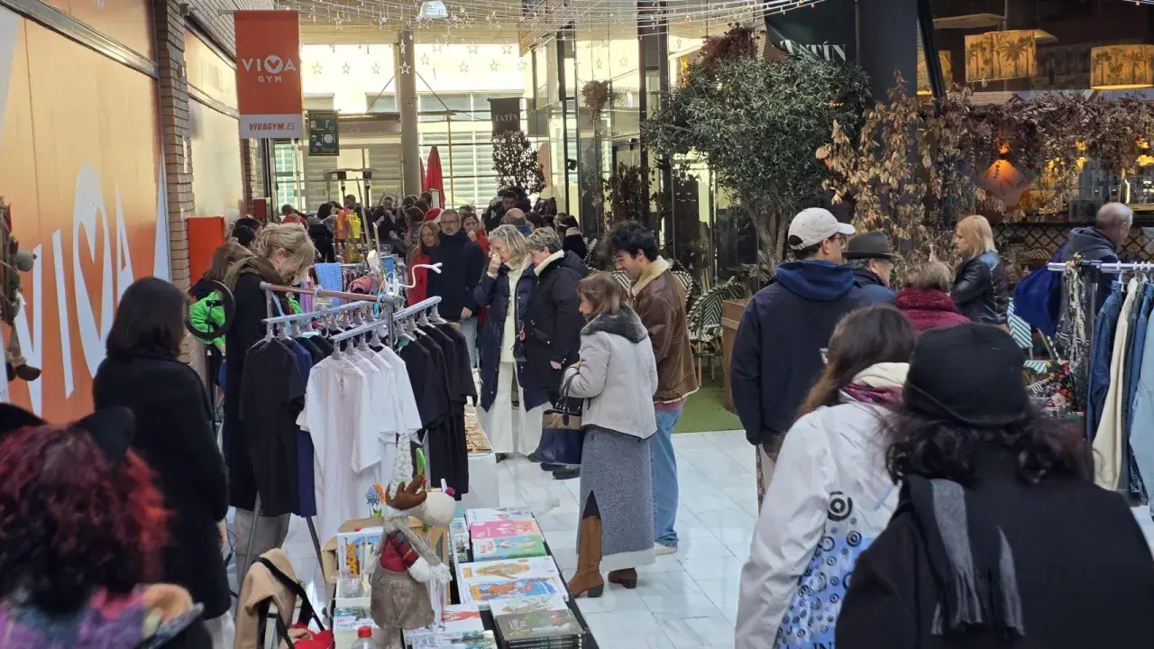 Gente comprando en un rastro de Zaragoza. Hay ropa colgada en percheros y puestos con libros y adornos.